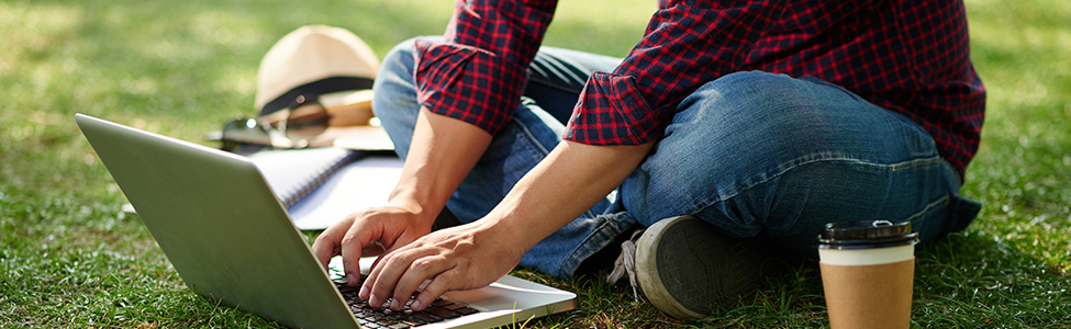 Person outside sitting on grass using laptop