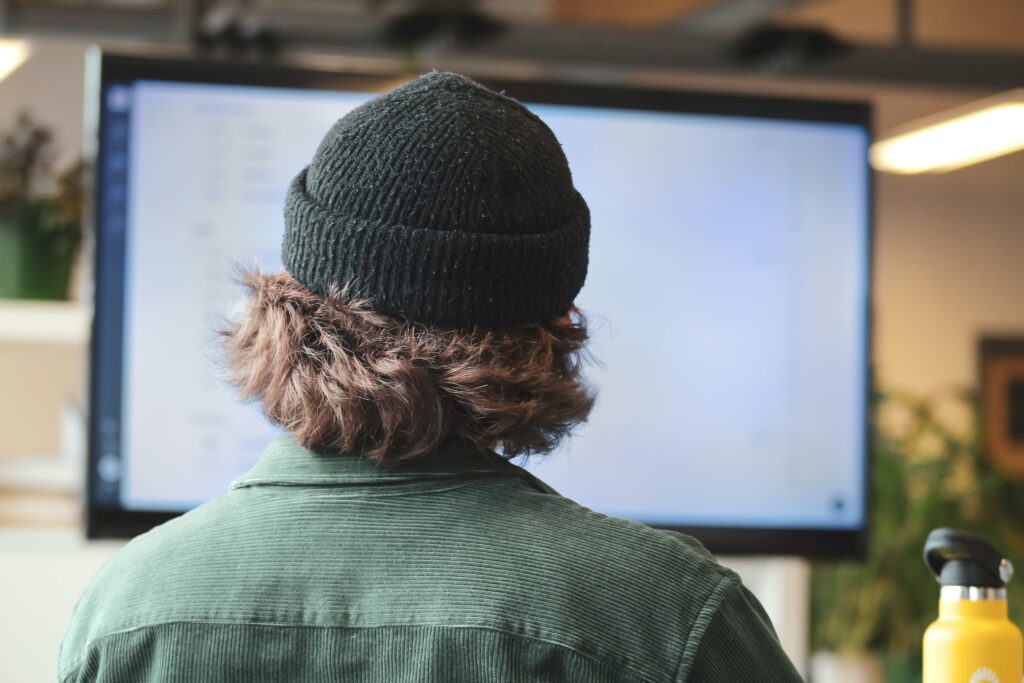 Person in green shirt wearing black knit cap looking at computer monitor